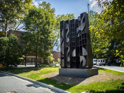 Large abstract steel sculpture with trees and campus buildings in background 