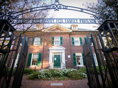 Exterior review of brick mansion with green shutters and distinctive iron gates